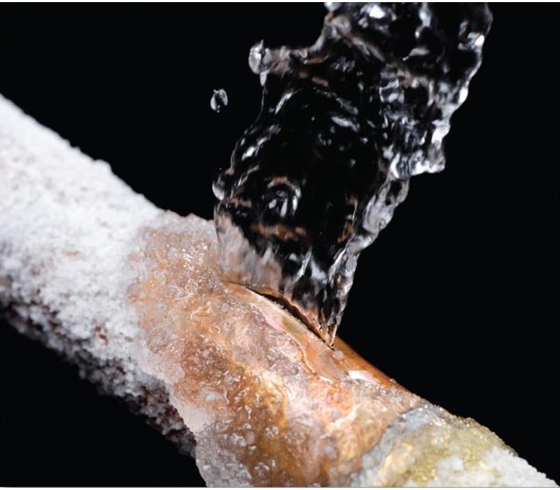 brass color pipe with white snow on it with water rushing out behind a black background